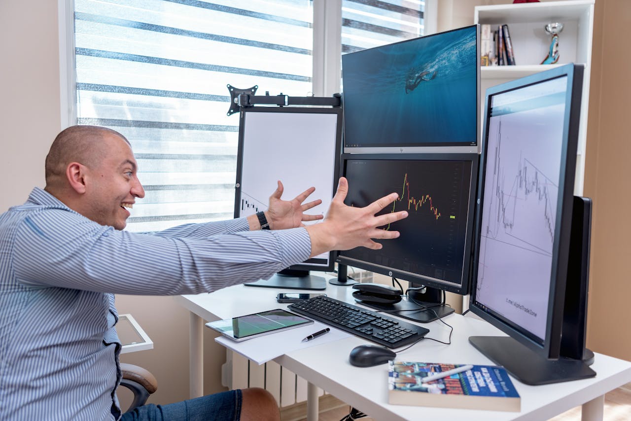 A joyful day trader celebrates a market victory in a modern office setup with multiple monitors displaying stock charts.