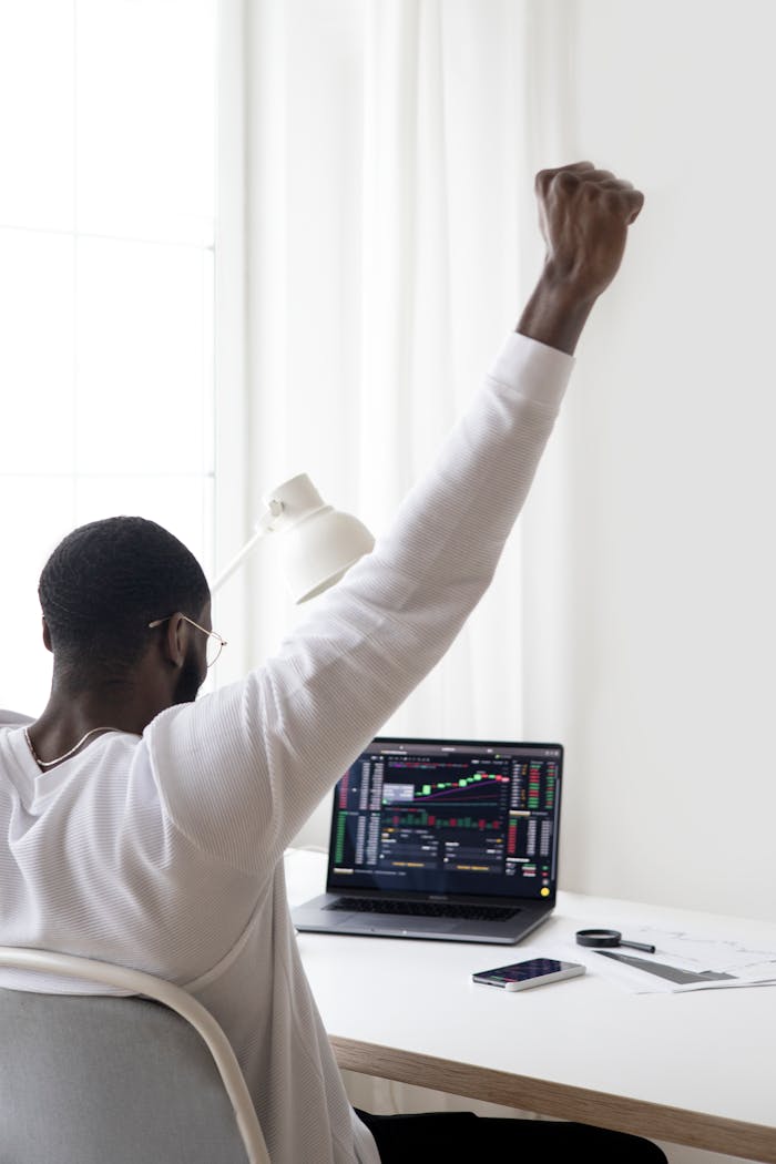 A man celebrates a successful stock market trade while sitting at his desk.